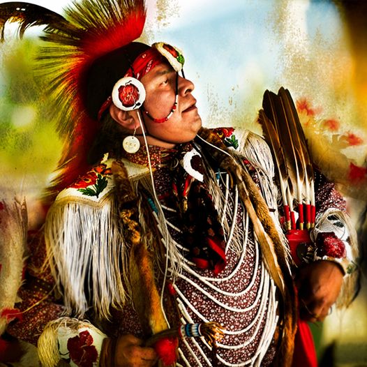 Colorful Native American Indian, side profile, mohawk haircut with feathers from ponytail, full traditional regalia.