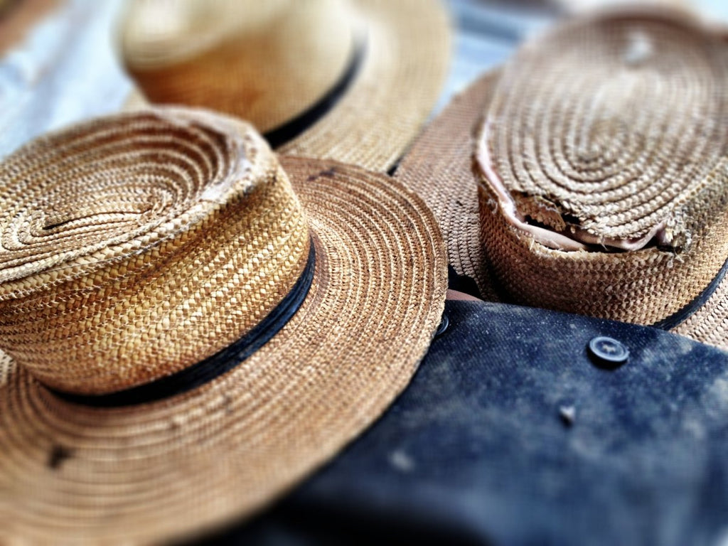 Three straw, brown amish hats scattered on a table with a blue denim jacket.