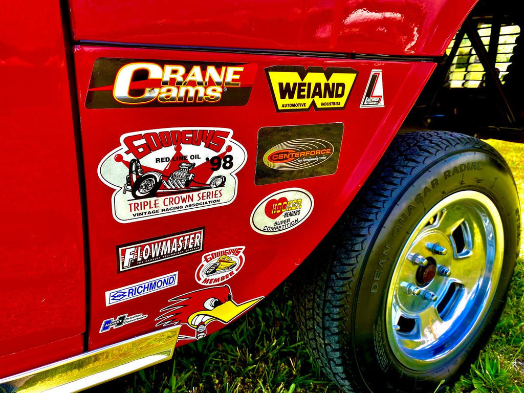 Colorful vintage racing stickers on red vehicle surface with chrome rim and tire