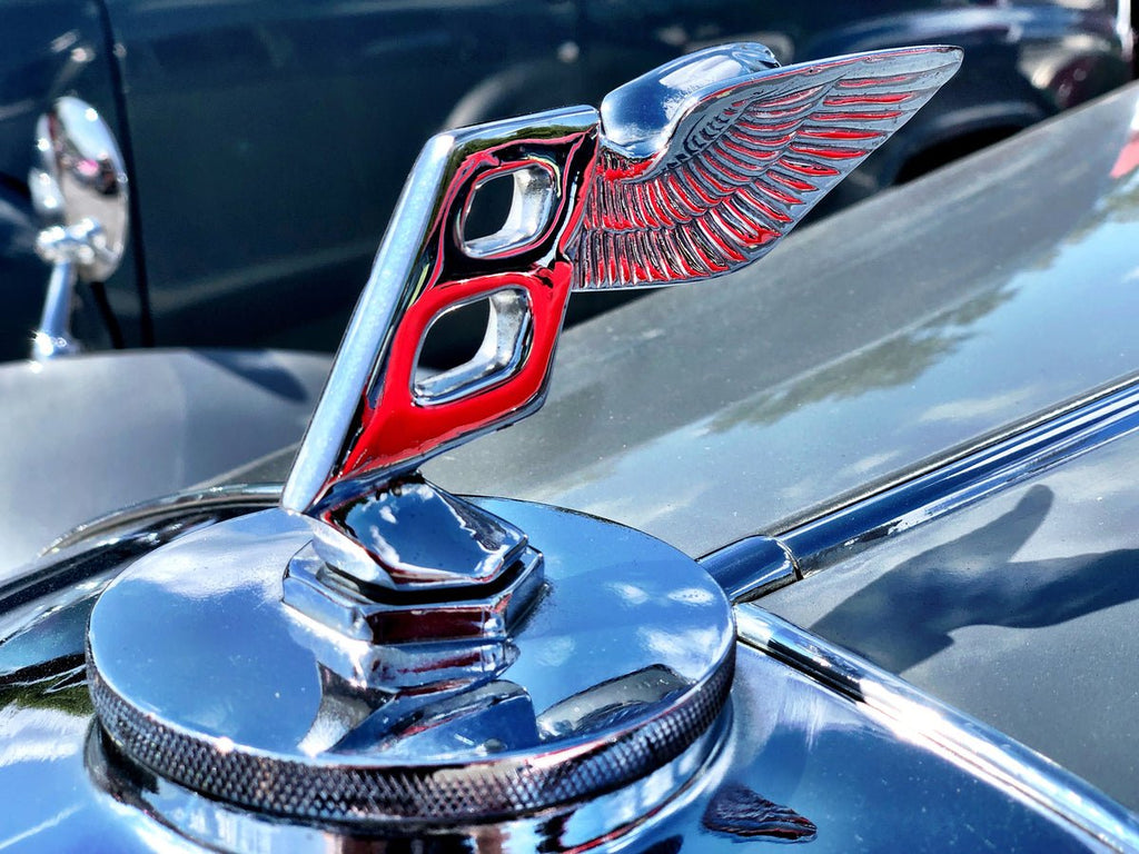 Close-up of Bentley Flying B emblem with chrome finish and red accents on hood