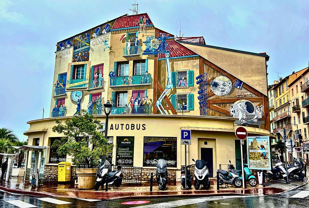 A colorful mural depicting movie scenes and space exploration covers the facade of a bus station in Cannes, France.