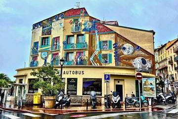 A colorful mural depicting movie scenes and space exploration covers the facade of a bus station in Cannes, France.