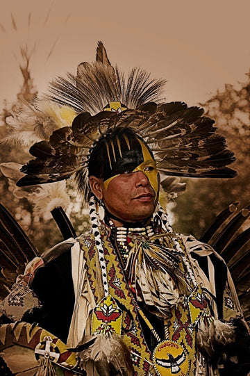 Native American, his headdress of feathers in a radiating pattern, face painted with black and yellow markings, wears a breastplate made of beads and bone.