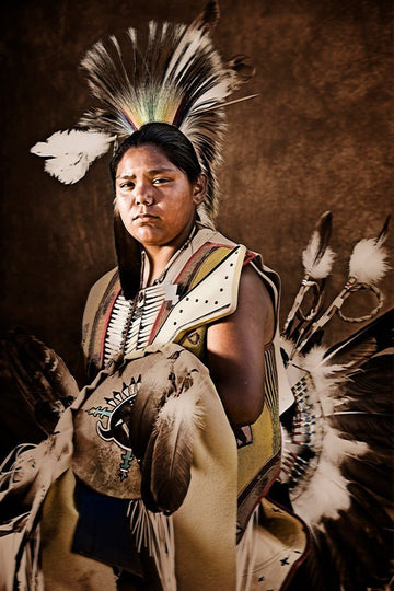 Young Indigenous American in traditional regalia with feather headdress, leather vest, and bone accessories, symbolizing cultural pride.