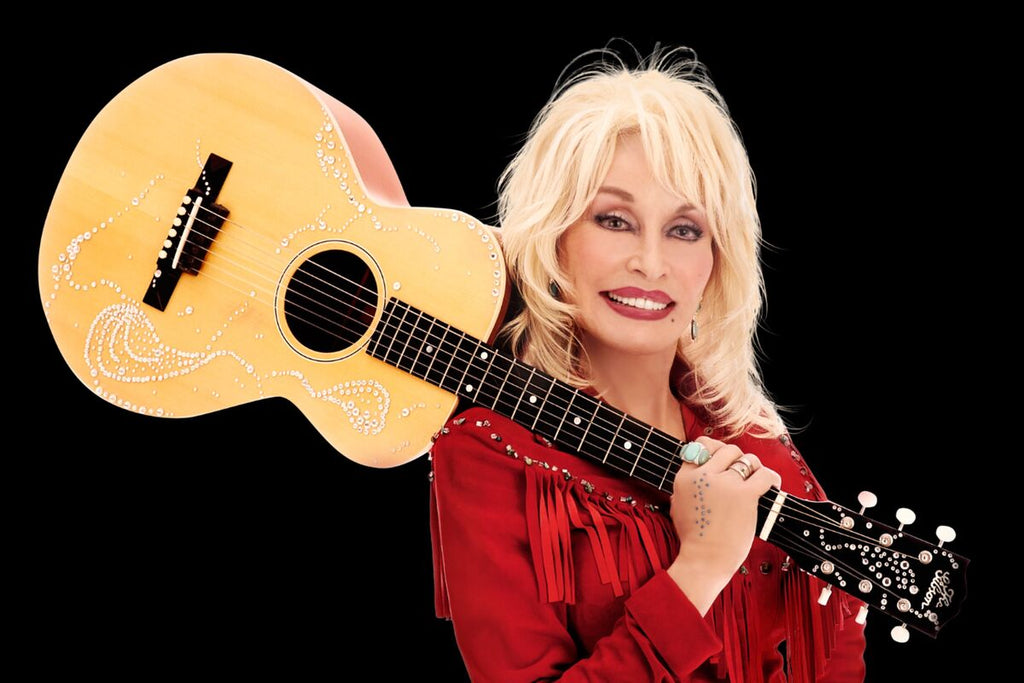 Dolly Parton holding acoustic guitar with rhinestones, wearing a red fringe shirt & turquoise ring against black background.