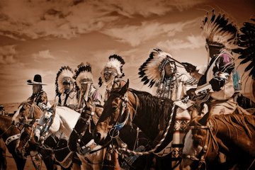 Native Americans on horseback in sepia tone, showcasing traditional regalia, photographed by Michael W. Rutherford.