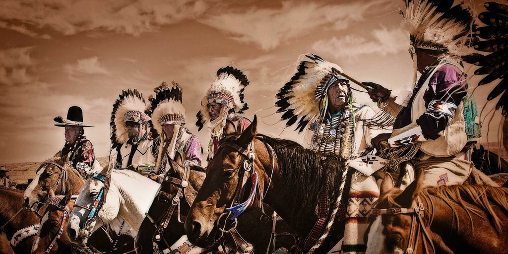 Native American chiefs in traditional headdresses atop horses beneath a cloudy sky in a sepia-look.