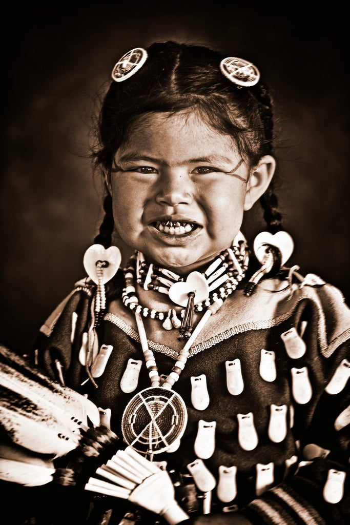 Sepia photo of Native American girl in traditional regalia, dancing with fan, bright expression.