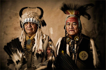 Two Native American elders dressed in regalia for a ceremonial occasion. Their faces, etched with experience and wisdom, convey a sense of dignity and strength. 