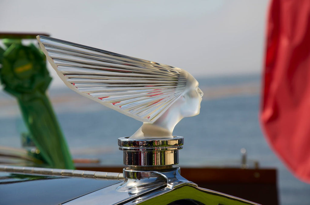 Lalique-inspired clear glass Victoire ornament on dark car hood, elegant design.