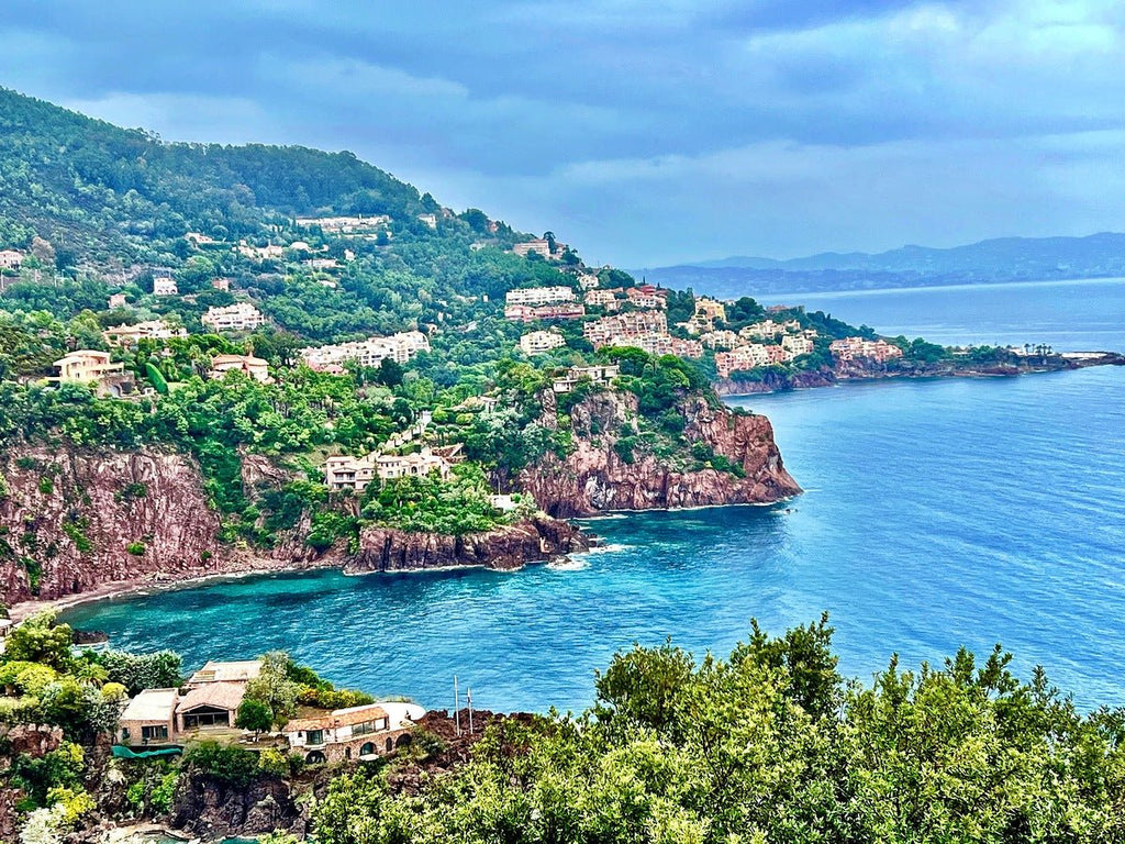 Art print of a French village on a cliff overlooking the Mediterranean Sea, with lush greenery and dramatic clouds post-storm.