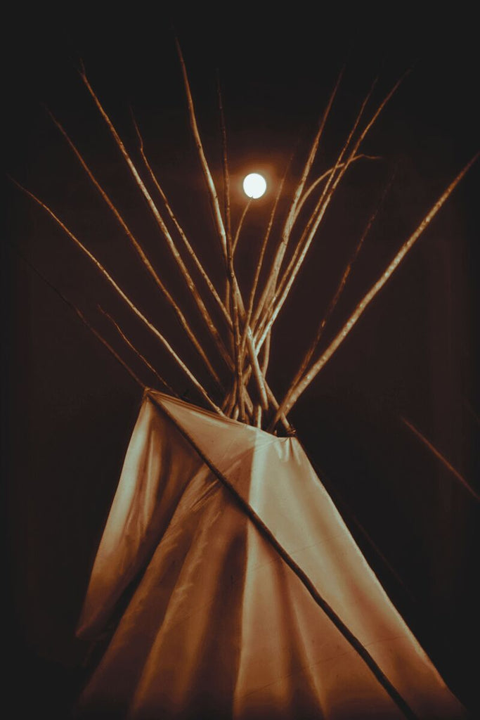 Limited edition print of a teepee illuminated at night, with a glowing interior and a full moon in the background, symbolizing Native American heritage.