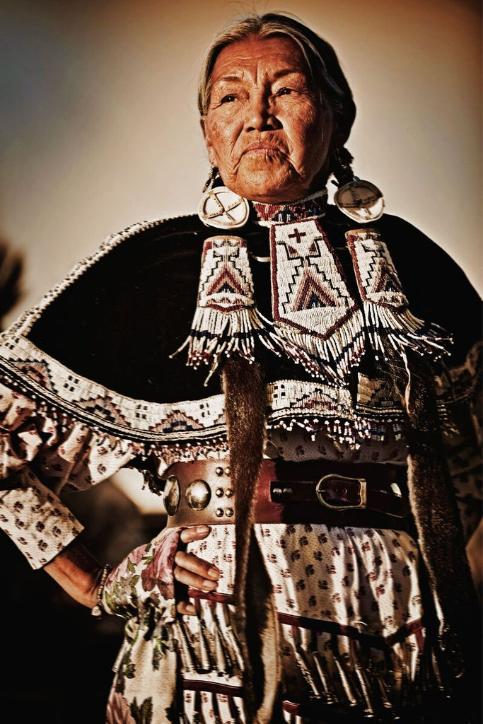 A Native American woman stands with her hand on her hip, exuding strength and dignity in elaborate traditional attire.