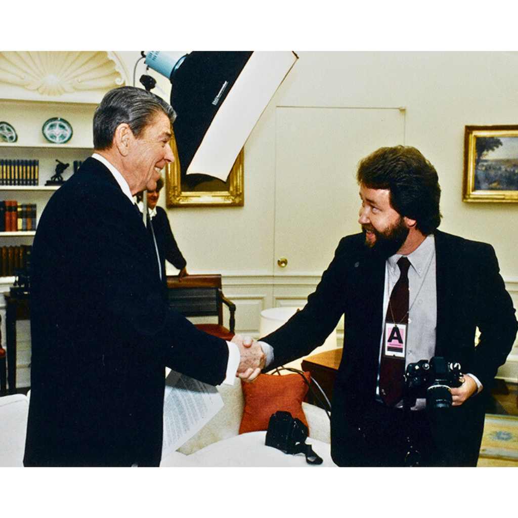 President Reagan shook hands with Michael W. Rutherford in the Oval Office, lighting in the background for a photo shoot.