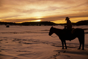 Lone cowboy on horseback in snow at sunset, limited edition print by Michael W. Rutherford.