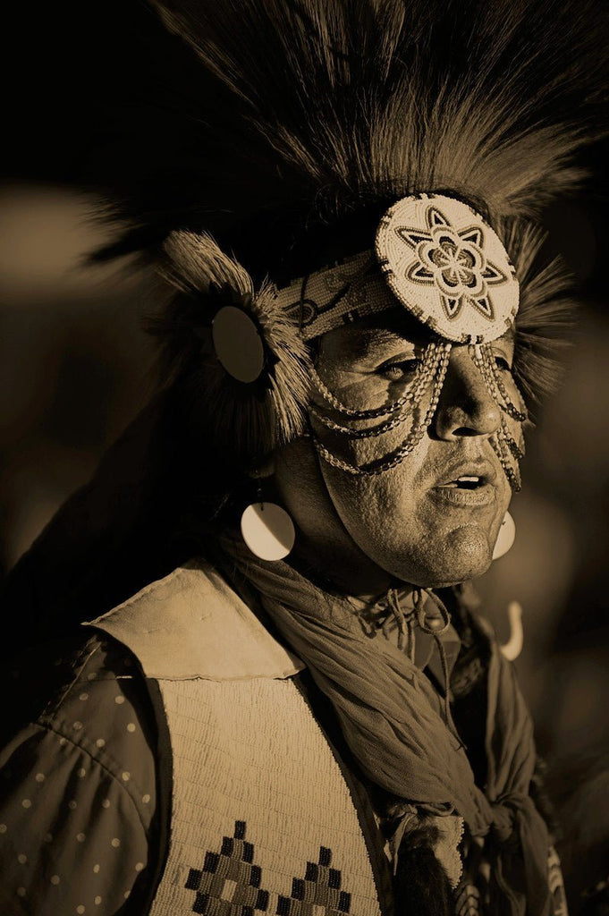 Native American in traditional regalia. His face is framed by an elaborate headdress of dark, thick fur or hair that extends outwards in a dramatic fashion.