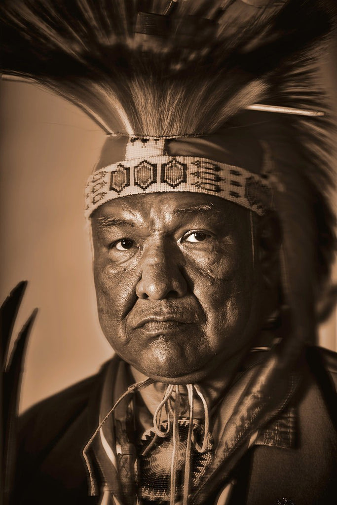 Native American, his gaze intense, conveying wisdom, strength, and solemnity. Wearing a traditional headdress, long feathers fanning out above his head,